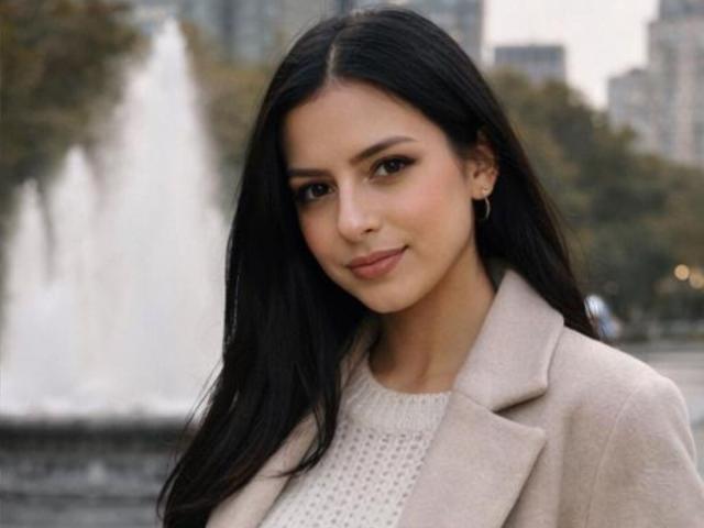 IsabellaJames has long black hair, brown eyes, and a slight smile. She wears a beige coat over a white knit top, with a small earring in her left ear.