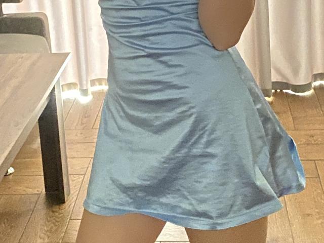 FlyFreedom's blue satin mini-dress, showing her bare thighs and a slight ass, stands in a wooden room with a table on the left. Her arms are partially visible.