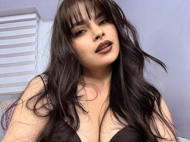 ClariceMontclair with long black hair, dark lipstick, and a black bra, showing her big tits in a selfie. She has a slightly open mouth and a confident look.