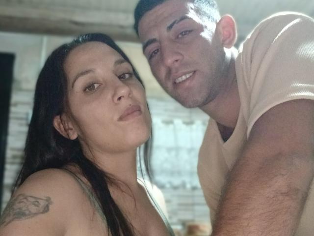 Maruli, con i capelli scuri e il seno piccolo, un tatuaggio sulla spalla, è appoggiata a Maruli, con i capelli corti neri, una maglietta bianca e una corporatura leggermente muscolosa, entrambe sorridenti..