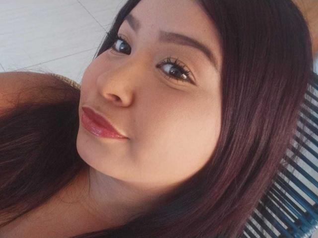 LenaCopers has smooth brown skin, dark brown eyes, long straight black hair, and glossy pink lips, smiling slightly. Her eyebrows are dark and well-groomed.
