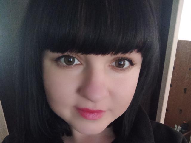 PattiLynn hat eine helle Haut, einen schwarzen, geraden Bob mit Pony, braune Augen und rosafarbenen Lippenstift. Ihre kleine Nase und leicht geschwollene Lippen sind sichtbar. Sie trägt ein schwarzes Oberteil..