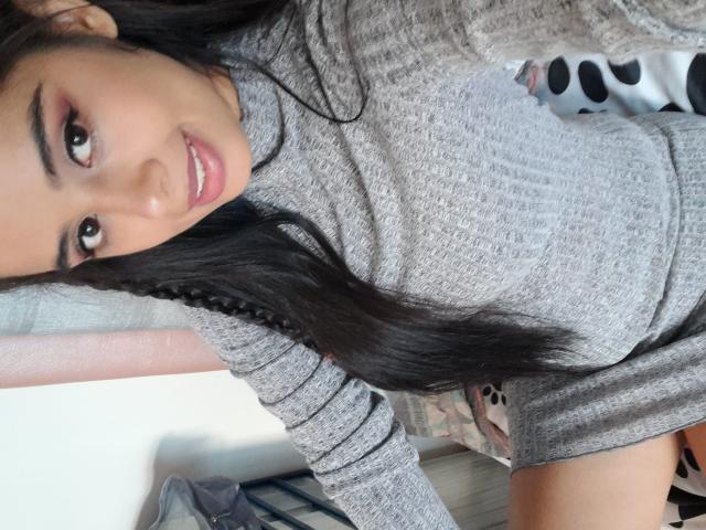 KeyklinOne a de longs cheveux noirs, elle porte un haut gris en maille côtelée, et on peut voir son joli sourire avec ses paupières roses. Ses petites seins sont visibles. Elle est agenouillée et regarde vers le haut..