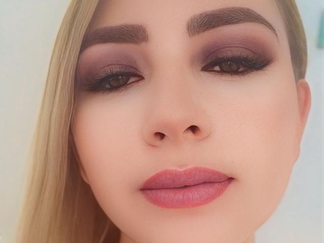 CristalWil's face, showing her pink lipstick, dark smoky eyeshadow, thick eyebrows, and long blonde hair. Her nose is small, and her eyes are half-open with black eyeliner.