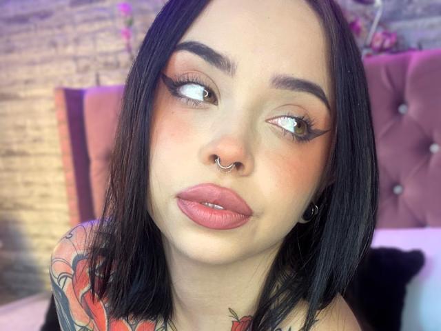 NaiaWhisper has black hair, brown eyes, and wears heavy eyeliner. She's got a nose ring, pink lips, and a tattoo on her shoulder. Boobless, no visible ass or pussy.
