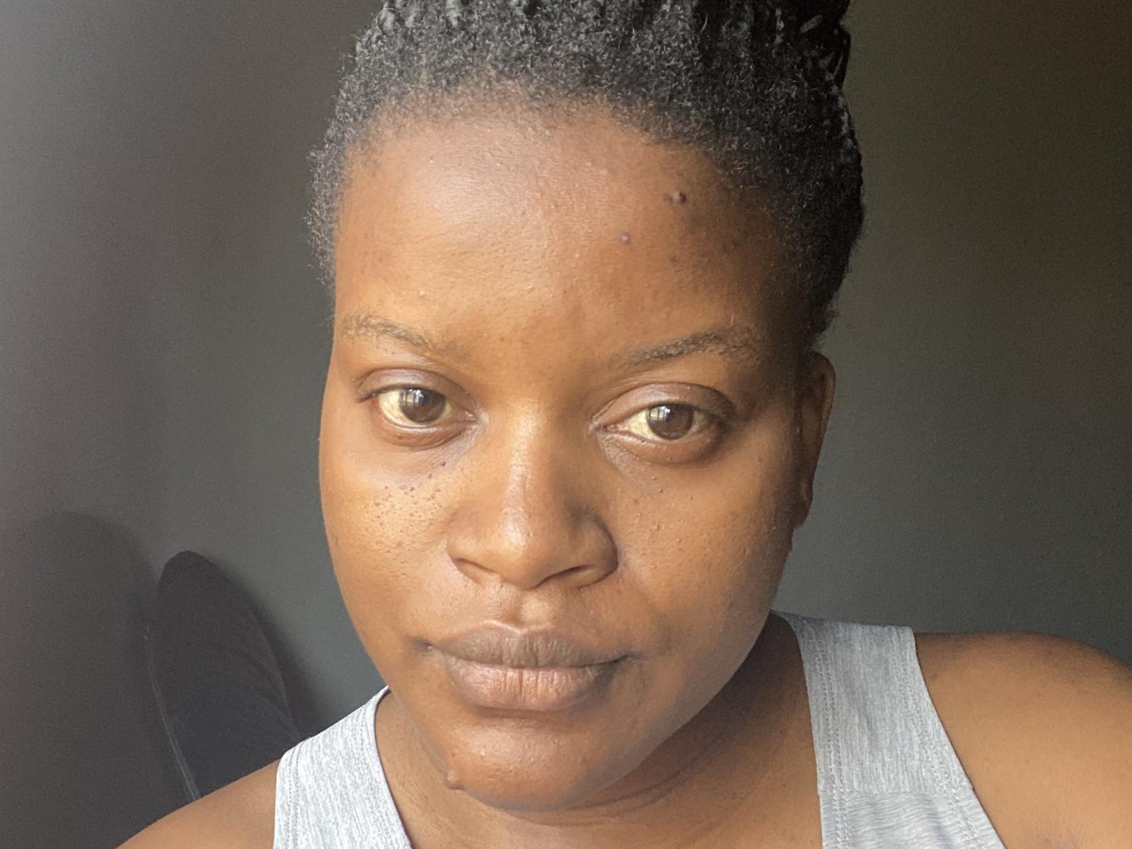 SassyLo has dark brown eyes, short curly black hair, and is wearing a gray tank top. Her brown skin is smooth with small freckles on her nose.