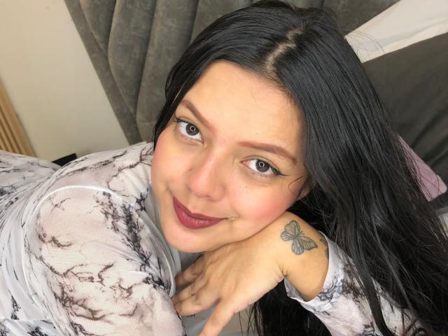 ViolettaRouse has black hair, blue eyes, and a butterfly tattoo on her right shoulder. She's wearing a white, black-marble-patterned top and smiling at the camera.