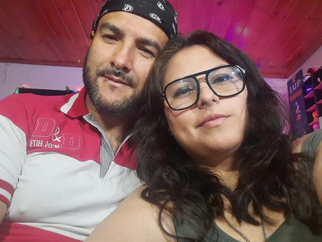 SektethLilith and her dude are in a selfie, she's got big tits and glasses, he's got a nose ring and bandana, both looking cute with a wood ceiling.