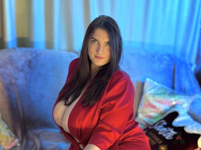 StephieRouse with large tits, wearing a red silk robe, sitting on a couch, long dark brown hair, blue lighting, slightly open robe showing cleavage, confident expression.