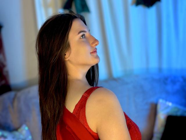 StephieRouse, avec de longs cheveux bruns, une robe rouge en dentelle, une peau claire, regardant par-dessus son épaule, un léger sourire, un éclairage bleu, l'épaule visible, le haut du dos, une lumière douce, une pose détendue..