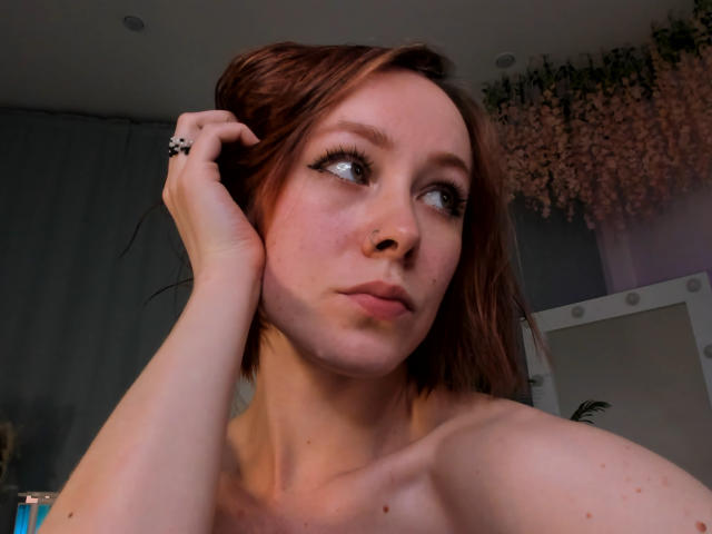 LilianKroft with red hair, fair skin, and blue eyes, looking up, pouty lips, nose ring, black ring, hand in hair, topless, freckles, soft lighting, subtle smile.
