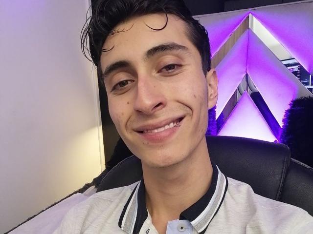 IthanSkin with a slight smile, brown eyes, and short dark hair, wearing a white shirt with black trim, showing a small cut on his lower lip.