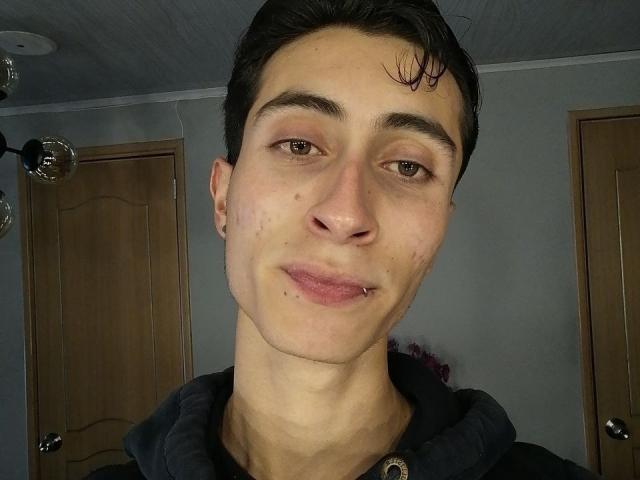 IthanSkin hat ein süßes, blasses Gesicht mit einer kleinen Nase, dunklen Augenbrauen und einem leichten Lächeln. Er trägt eine schwarze Kapuzenjacke, und sein nasses, dunkles Haar ist teilweise nach hinten gekämmt..