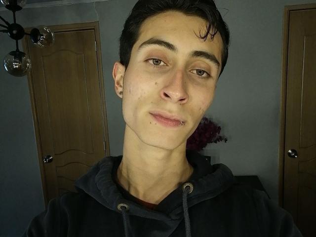 IthanSkin, un homme mince avec des cheveux foncés et un petit piercing au nez, porte un sweat à capuche noir et regarde la caméra avec un léger sourire. Sa peau est claire..
