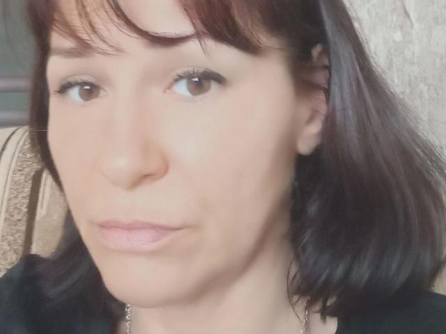 MonicaErotisch-hot has pale skin, brown eyes, and dark brown shoulder-length hair with bangs. She has light pink lipstick and a slightly pouty expression. Her face is centered in the image.
