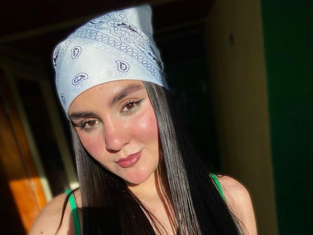 ValeryDuran has long black hair, wearing a blue bandana with white patterns, green top, and a slight smile. Sunlight highlights her pink cheeks and brown eyes.