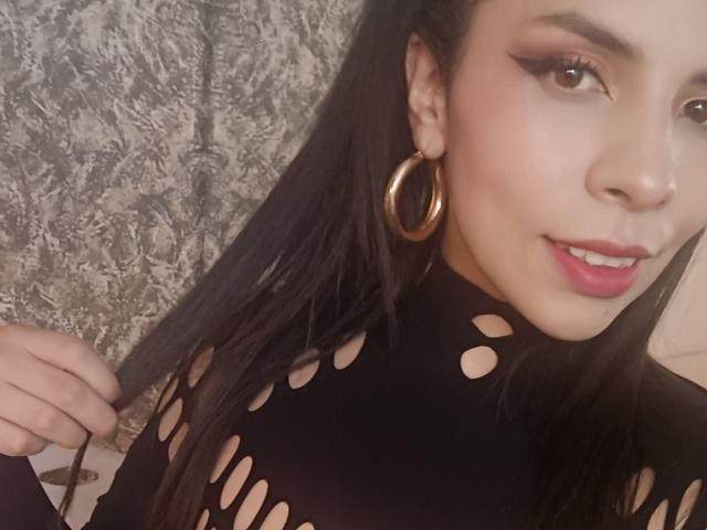 VioletaStone with long black hair, wearing a black cut-out top, hoop earrings, and red lipstick, smiling with a nose ring, holding her hair. Her tits are not visible.