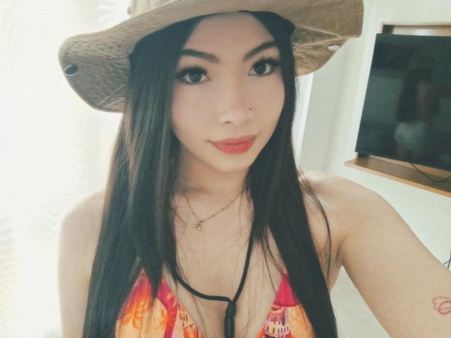 ViolettaLeroy with long black hair, wearing a straw hat, red lipstick, and a colorful bikini top, showing her tits and a small tattoo on her right arm.