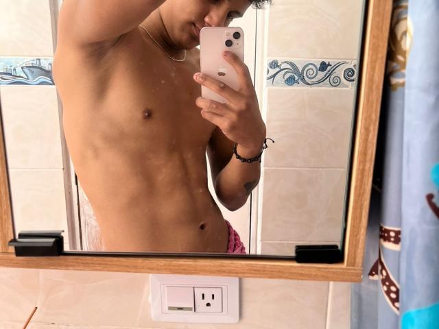 Una selfie en el espejo de JamessHott sin camisa, con un cuerpo tonificado y delgado, abdominales visibles y ropa interior rosa, sosteniendo un teléfono rosa, en un baño..