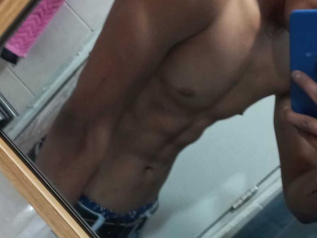 Autoportrait de JamessHott montrant sa musculature, torse nu, avec des abdominaux et des pectoraux bien définis, portant des sous-vêtements bleus et blancs, tenant un téléphone bleu, avec un bras et une tête partiellement visibles..