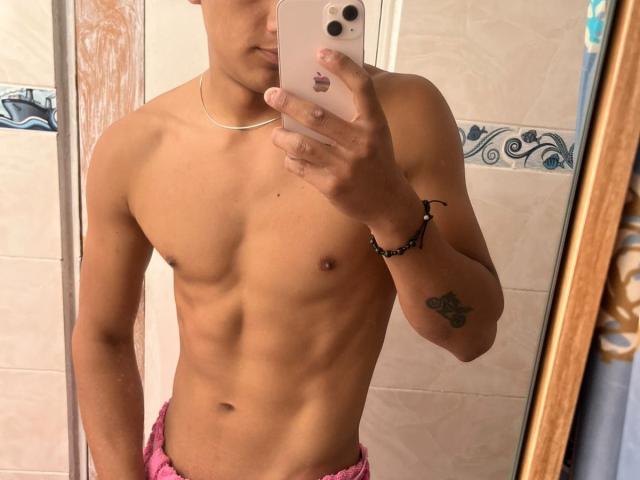 Shirtless JamessHott with a slim, toned physique, small nipples, and a tattoo on his right arm, taking a mirror selfie, wearing pink shorts, holding a pink iPhone.