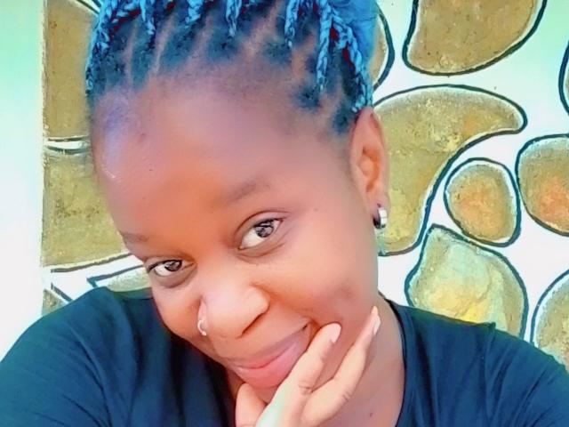 SexyBrexy with blue dreadlocks, nose ring, and black shirt, smiling and resting chin on hand, looking cute and attractive.