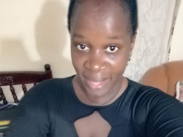 SexyBrexy with dark skin, short black hair, and a small smile wearing a black top with a cutout. Her eyes are looking at the camera.