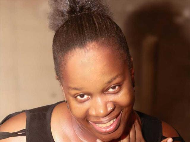 SexyBrexy with dark brown skin, short curly Afro, smiling widely, black sleeveless top, nose ring, and cute earrings, showing off her shiny teeth and playful expression.