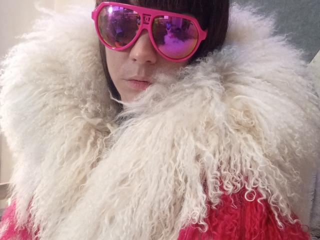 OrianaLaFrancaise wearing pink reflective sunglasses, fluffy white fur collar, and red jacket, with a serious expression, brown straight hair, and fair skin.
