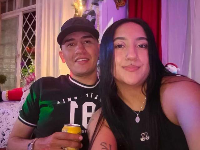 TemptationDual con capelli scuri, piccolo piercing al naso, top nero senza maniche e collana, sorridente accanto a TemptationDual in una maglia sportiva verde, cappello nero, che tiene una bevanda gialla, illuminazione viola..
