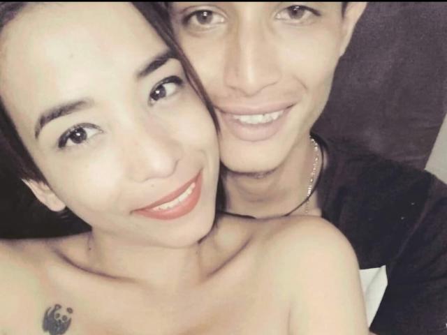 AlejoyMaria with small tits, tattoos, and brown hair, smiling next to AlejoyMaria with short brown hair, smiling, showing neck tattoo and bare shoulders.