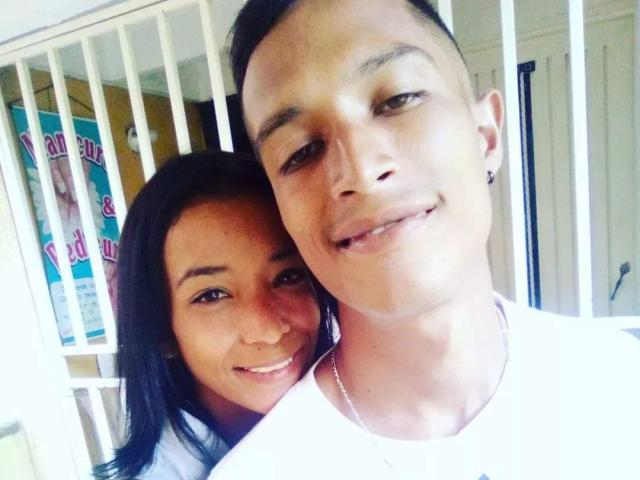 AlejoyMaria with short black hair, smiling, has a small nose ring and wears a white shirt. AlejoyMaria with long black hair, smiling, rests her head on his shoulder.