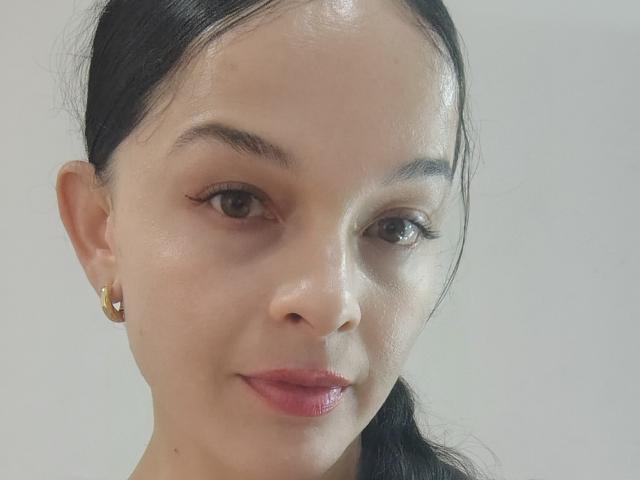 LatinaCulChaud has fair skin, black hair in a ponytail, brown eyes, red lips, and gold earrings. Her face is slightly shiny, with a neutral expression.