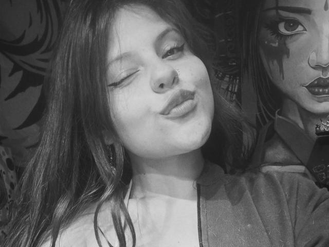 Black-and-white selfie of SophieHill with one eye closed, winking, nose ring, and long hair, wearing a hoodie, next to a partially visible, heavily-styled portrait of another girl.