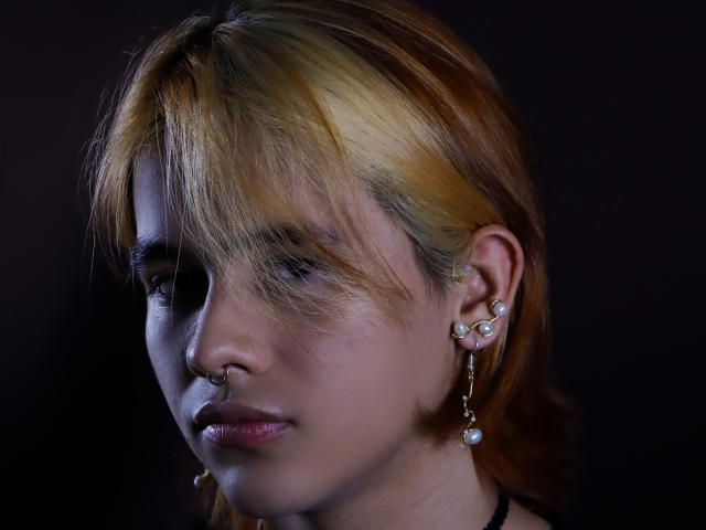 BenjiVampire has dirty blonde hair, a nose ring, and multiple ear piercings with dangling jewelry, against a dark background. BenjiVampire's face is slightly shadowed, with a serious expression.