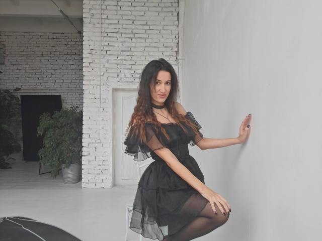 BanyReid with long brown hair, wearing a black sheer dress, off-shoulder, black choker, and black stockings, kneeling, touching white wall, smiling, sexy, cute, attractive.