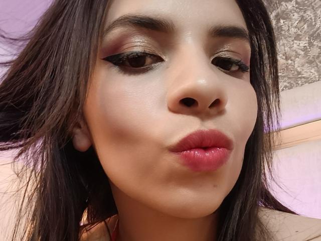 VioletaStone's pouty ass-face, with glossy pink lips and thick black eyeliner, her brown eyes half-closed, long dark hair, and pale skin, in a tight selfie.