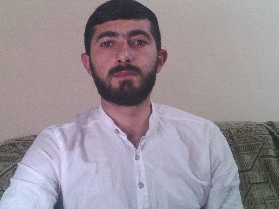 KingLoned has a thick black beard, short dark hair, and is wearing a white button-up shirt. His brown eyes and neutral expression are visible.