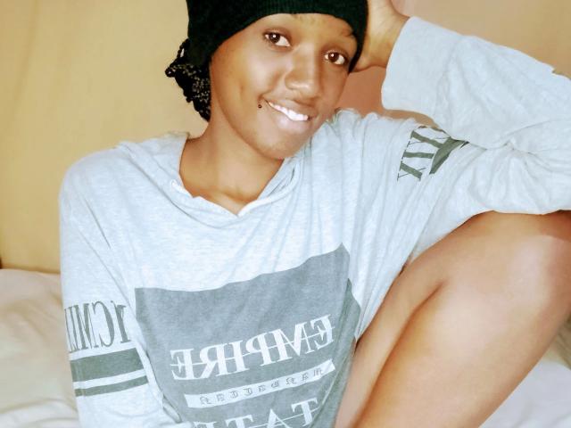 EbonyShy-hot with dark skin, smiling, wearing a green beanie, gray hoodie, and black shorts, sitting with one leg up, showing her bare thigh and cute gold tooth.