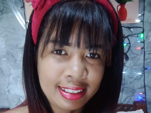 MariahSquirting69 has black hair, red headband, and red lipstick, smiling with pink lips. Her Asian skin is smooth, and she's looking at the camera. Her tits are not visible.