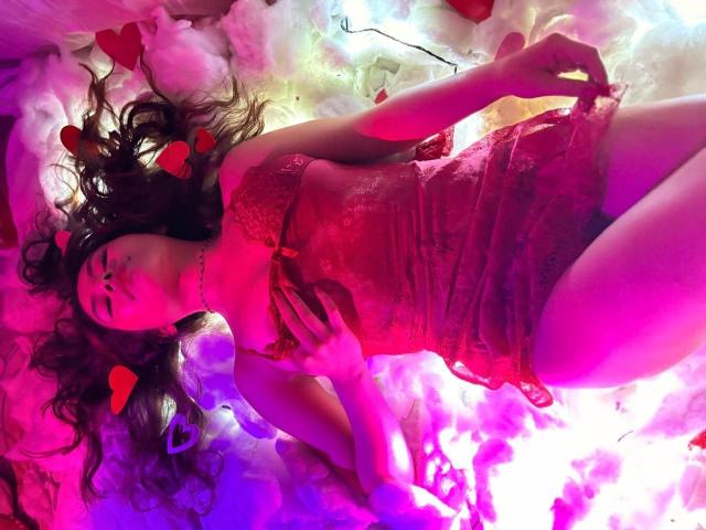 AliceEvansLove lying on pink and white fluffy clouds, wearing a red lace babydoll, with purple and pink lights, heart stickers, and her dark wavy hair spread out.