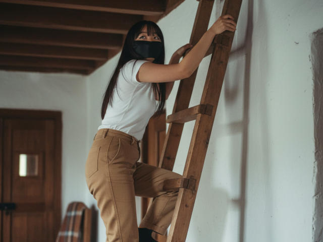 BeloverNana climbing a wooden ladder, wearing a black mask, white shirt, and tan pants, with her ass slightly raised, looking back with serious eyes.