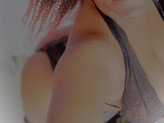 Close-up of Randyxboom's upper body, focusing on her right shoulder and part of her face. She has light brown, curly hair. She's wearing a black lace bra, which is slightly pulled to the side, revealing part of her right breast. The image is slightly blurred, emphasizing the texture of her lace bra and the softness of her skin. The background is out of focus. The composition highlights her upper body and the lace's delicate pattern.