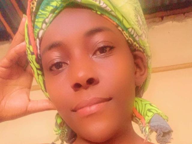 FaithyTotoo has a cute, brown-skinned face with shiny skin, small nose, and subtle smile. She's wearing a green headscarf with colorful patterns, and her hand's in the frame.