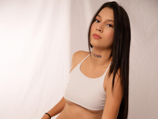 CloeThonsom with long black hair, wearing a white sports bra, showing small tits, tan skin, subtle tattoo on neck, slight smile, looking at camera, white background.