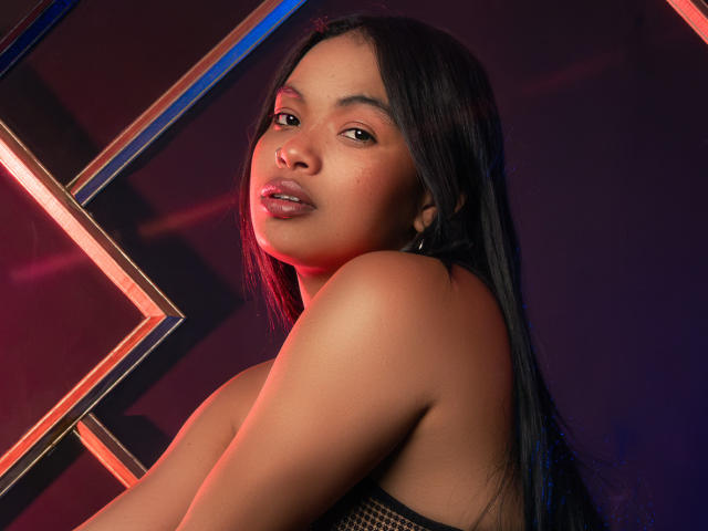 SoleneFontaine with long black hair, looking over shoulder, showing bare shoulders and upper tits, dark skin, pink lips, subtle makeup, neon red and blue light in background.