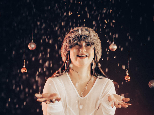 MelindaBoobs with wet white shirt, fur hat, smiling, arms out, water droplets, wearing necklace, Christmas ornaments hanging, dark background, brown hair, soft light, happy expression.