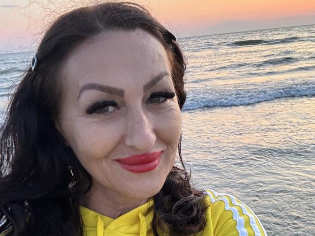 AfriDetta has red lips, dark wavy hair, and thick eyebrows. She's smiling at the camera with a yellow shirt, wearing hoop earrings, and has a sexy, attractive face.