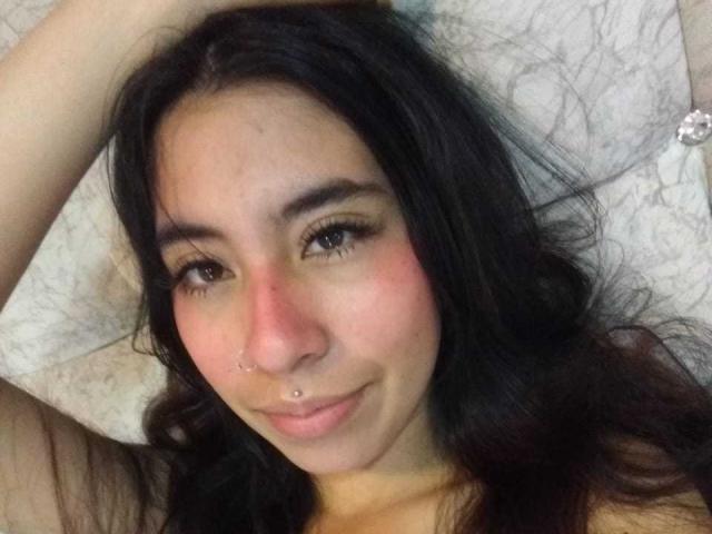 LinaSpearce has dark hair, a nose piercing, and a slight smile. Her brown eyes are half-open, and she has a red nose. She's lying on a white pillow.