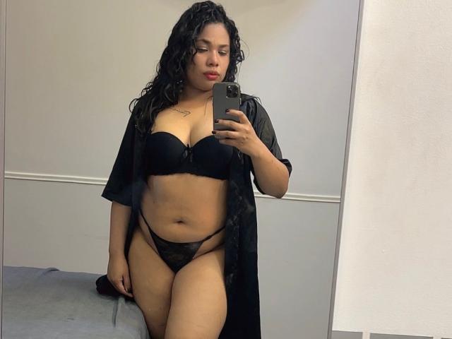 VanessaFory with curly black hair, wearing black bra and sheer black robe, black thong, showing her ass and pussy, holding phone, mirror selfie, light skin, red lipstick.